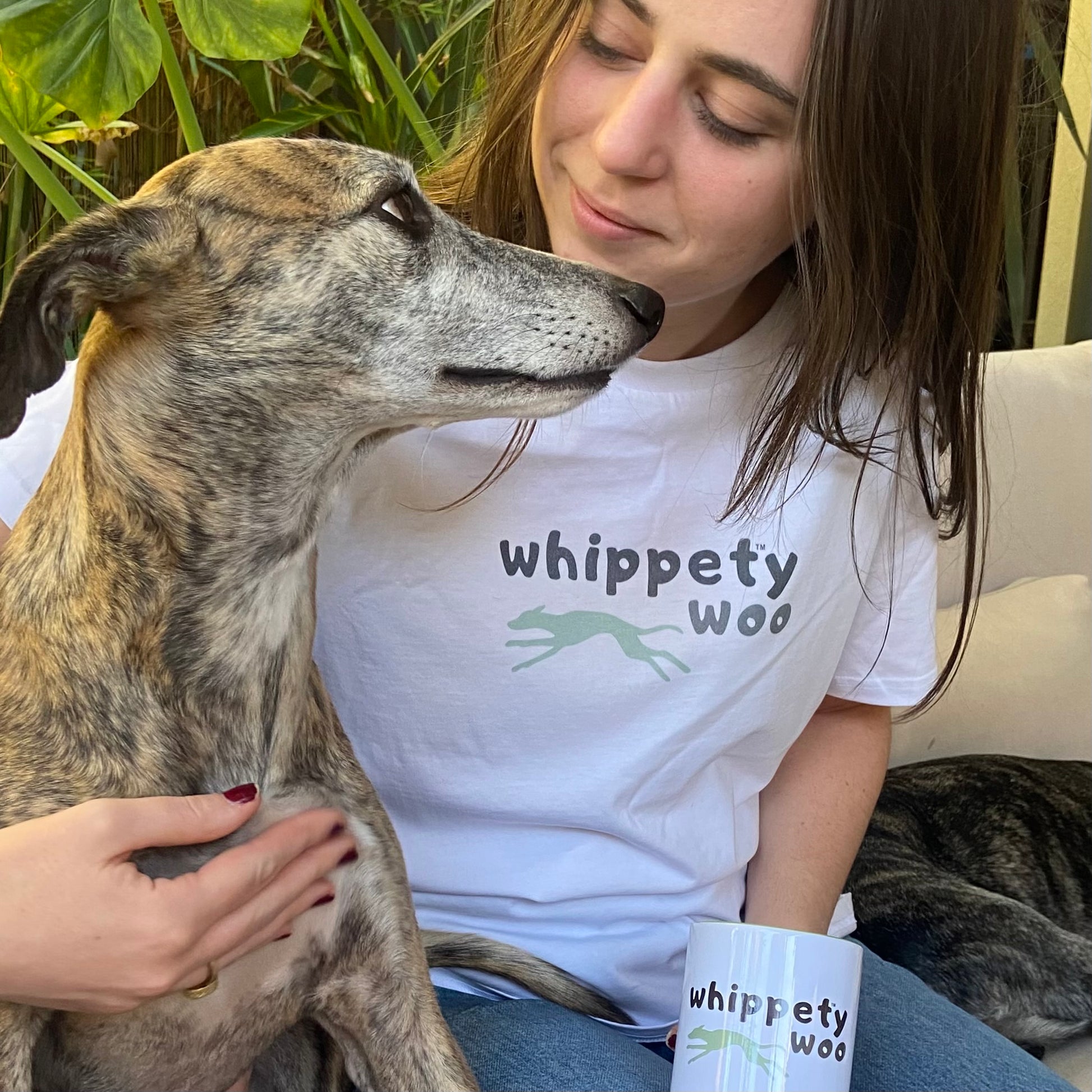 Young woman wearing a 'whippety woo' t-shirt sitting with a whippet.