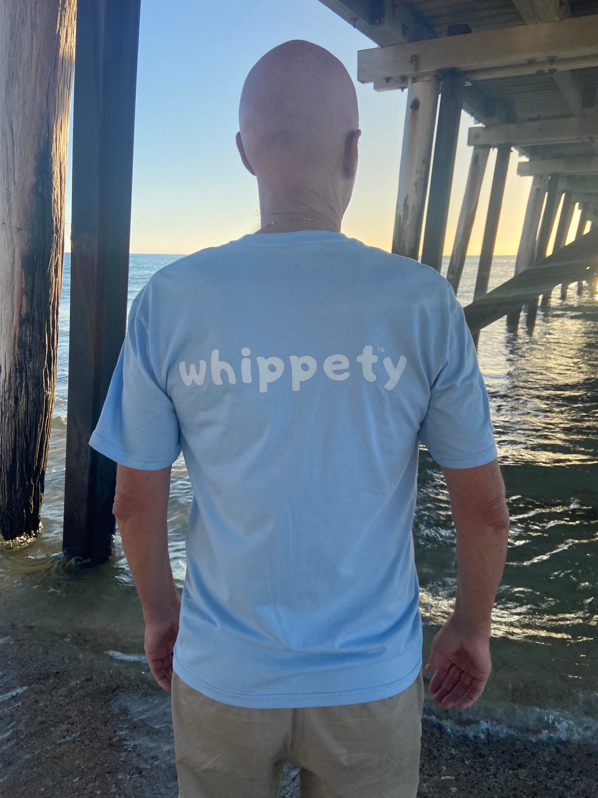 Man wearing a light blue t shirt with 'whippety' logo by sea edge