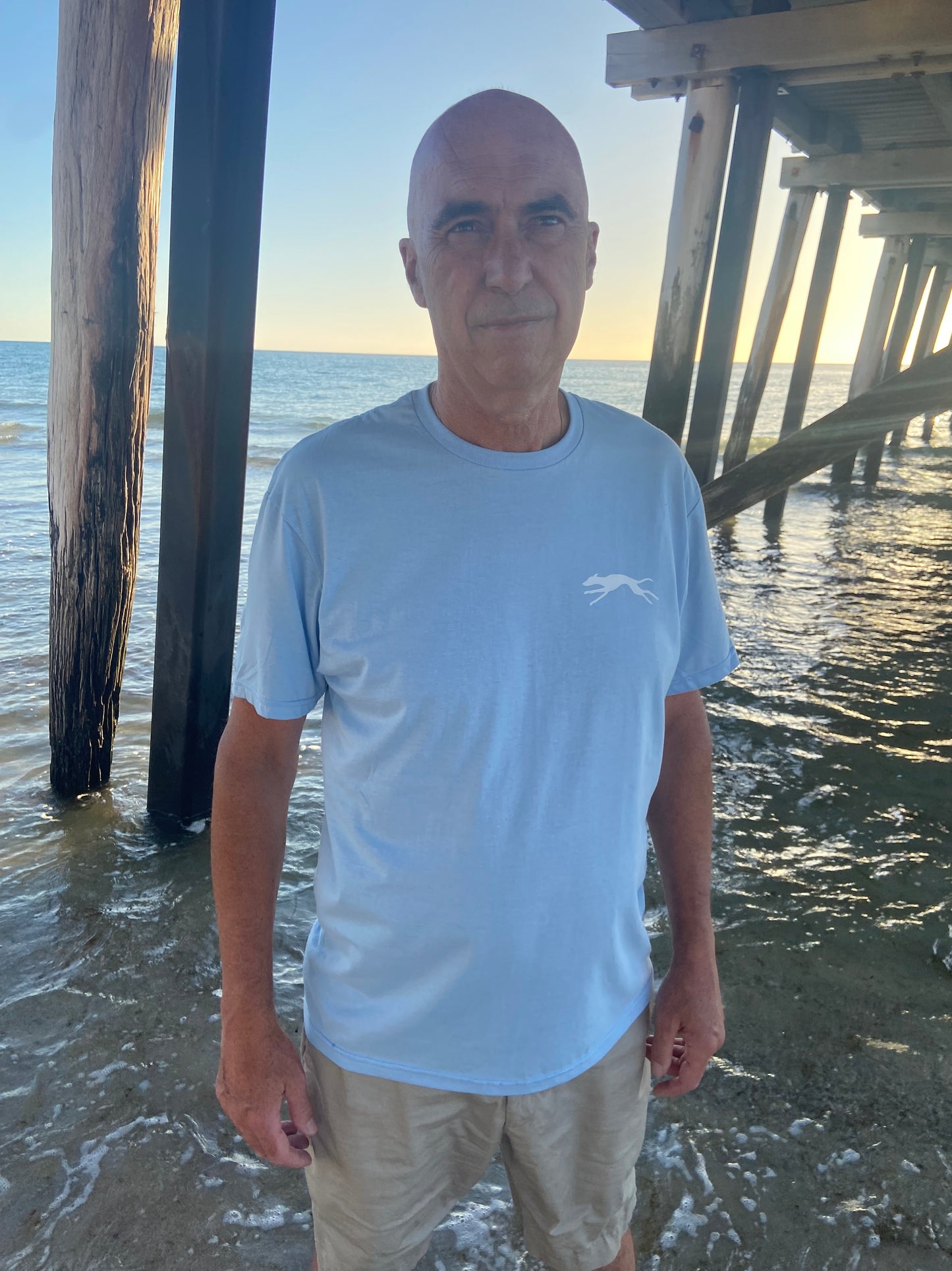 Man standing by sea wearing a blue t  shirt and beige pants